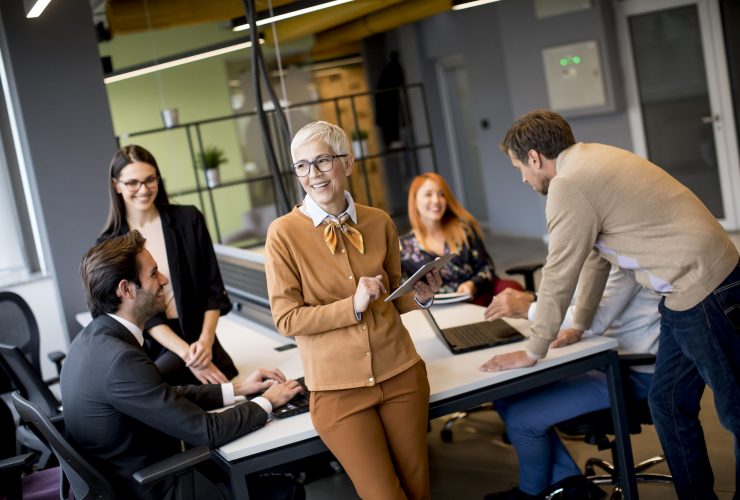 Group of business people working and communicating while standing in  the office together with colleagues sitting in the background